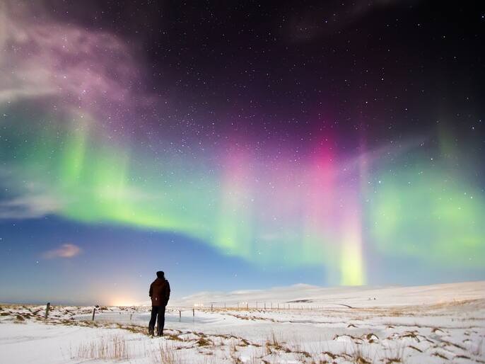 Man looking at Aurora Borealis in north Iceland.Snow covered ground with stars and Northern lights dancing in the sky.
