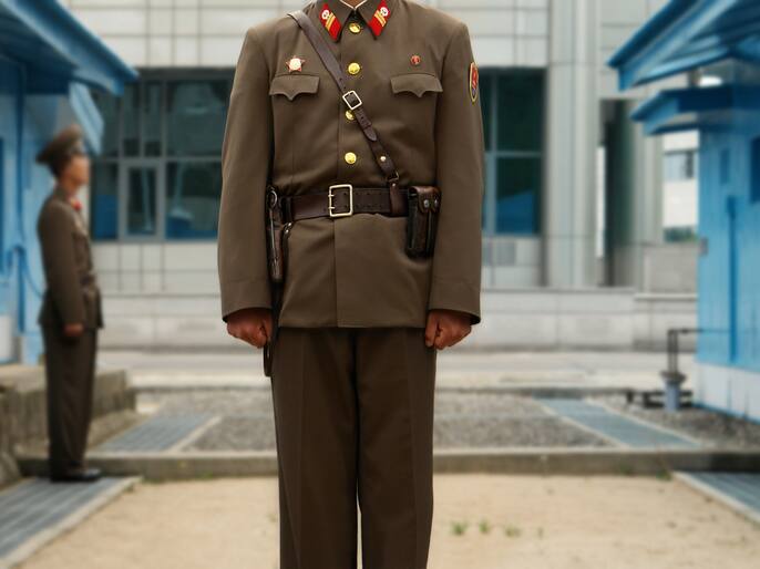 Unique View From North Korean Side: North Korean Soldiers guard the border between South and North marked by a short concrete wall. Focus on the Soldier in the Middle, Background Out of Focus.