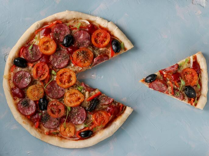 Pizza with a cut out piece on a light blue background, top view